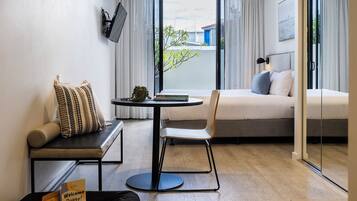 Una habitación de hotel moderna con sofá, una mesita redonda, cama y televisor montado en la pared.