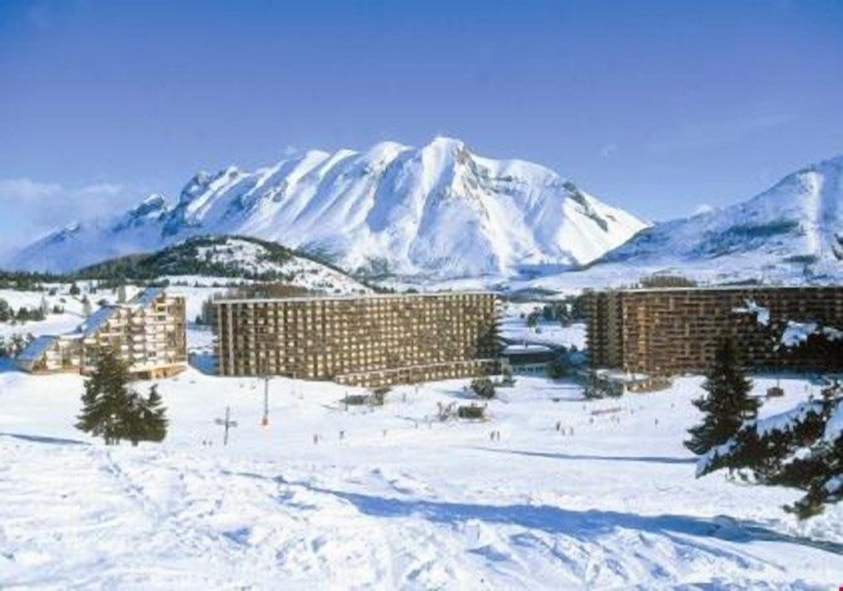 A snow-covered landscape with a mountain in the background and a building with multiple floors in the foreground.