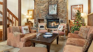 A cozy living room with a stone fireplace, wooden furniture, and a Christmas tree. - Steps from Shuttle, Garage, 4 Bedroom + Basement, Private Scenic Setting (Vail)