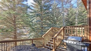 A deck with a grill and a round table, surrounded by trees. - Steps from Shuttle, Garage, 4 Bedroom + Basement, Private Scenic Setting (Vail)