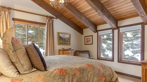 A bedroom with a large bed, wooden beams, and two windows with views of trees. - Steps from Shuttle, Garage, 4 Bedroom + Basement, Private Scenic Setting (Vail)