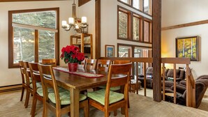 A dining area with wooden furniture, a chandelier, and large windows. - Steps from Shuttle, Garage, 4 Bedroom + Basement, Private Scenic Setting (Vail)