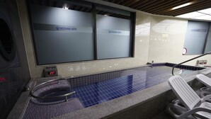 Moderni sisäuima-allasalue, jossa on digitaalinen lämpömittari, joka näyttää 20 °C:n lämpötilan, lasiseinä, jossa on merkintä ”Ocean Spa”, ja laatoitettu lattia.