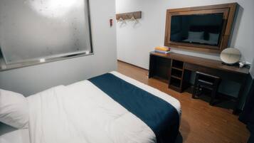 Una habitación de hotel con una cama, un escritorio con espejo y un televisor.