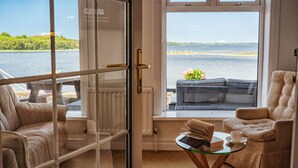 Een kamer met uitzicht op een meer, een bank, een stoel, een glazen tafel met een boek en een kopje, en een raam met uitzicht op het meer.