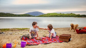 Een strandscène met twee spelende kinderen, een hond en een picknick.