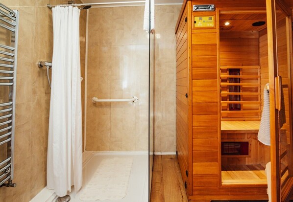 Ducha con mampara de vidrio, una toalla blanca y una sauna de madera con panel de control.