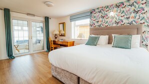 Een slaapkamer met een groot bed, een bureau en een stoel. Er is een raam met gordijnen en uitzicht op buiten.