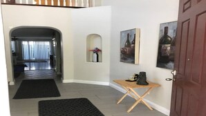 Un corridoio con una porta in legno, un tavolino con una bottiglia e due quadri appesi al muro.