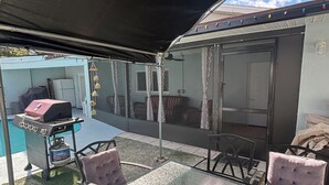 Um pátio externo com mesa e cadeiras, churrasqueira e área coberta com vista para o quintal.
