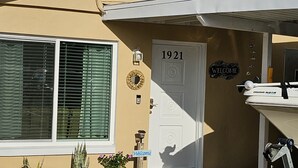 Uma casa com uma grande janela, uma porta com a inscrição "1921", uma placa de boas-vindas e uma caixa de correio.
