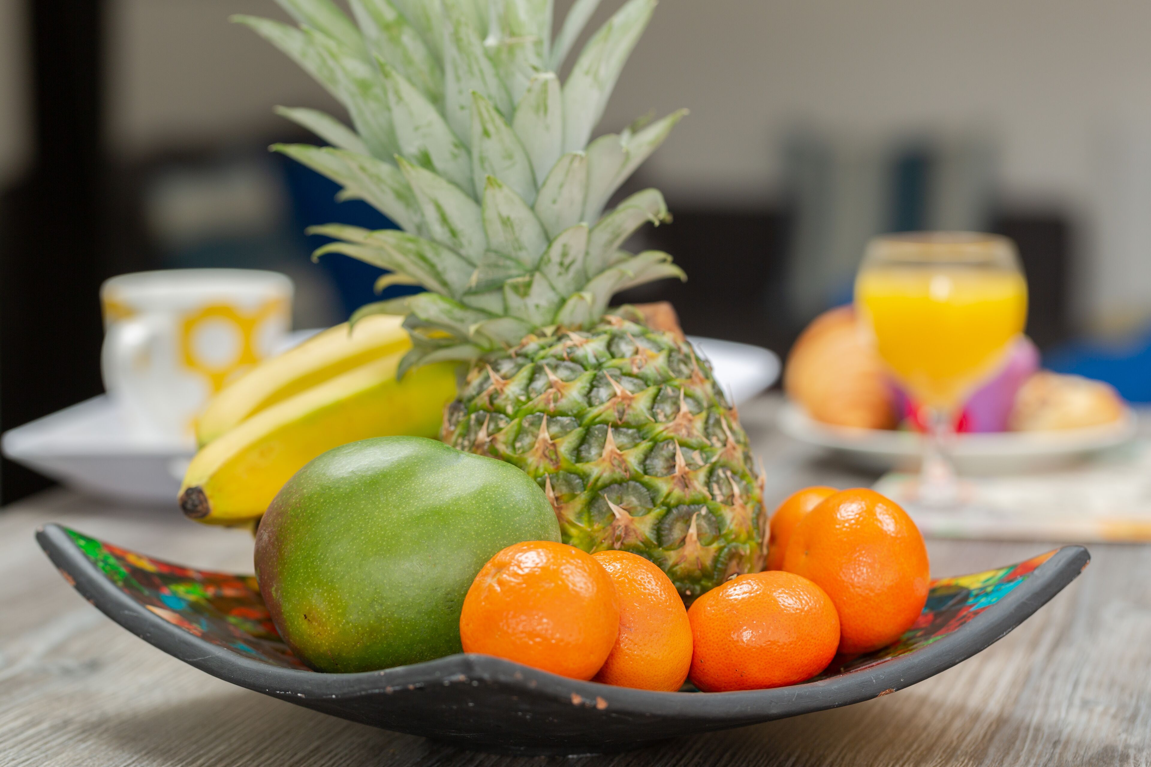 A bowl of fruits including a pineapple, mango, and oranges on a table.