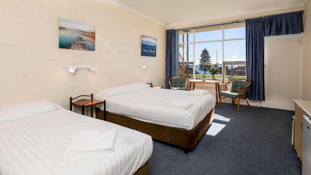 A hotel room with two beds, a desk, a chair, and a large window with a view of a dock and trees. - Blue Seas Motel (Port Lincoln)