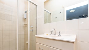 A modern bathroom with a glass shower enclosure, a white sink with two faucets, and a mirror above the sink. - Blue Seas Motel (Port Lincoln)