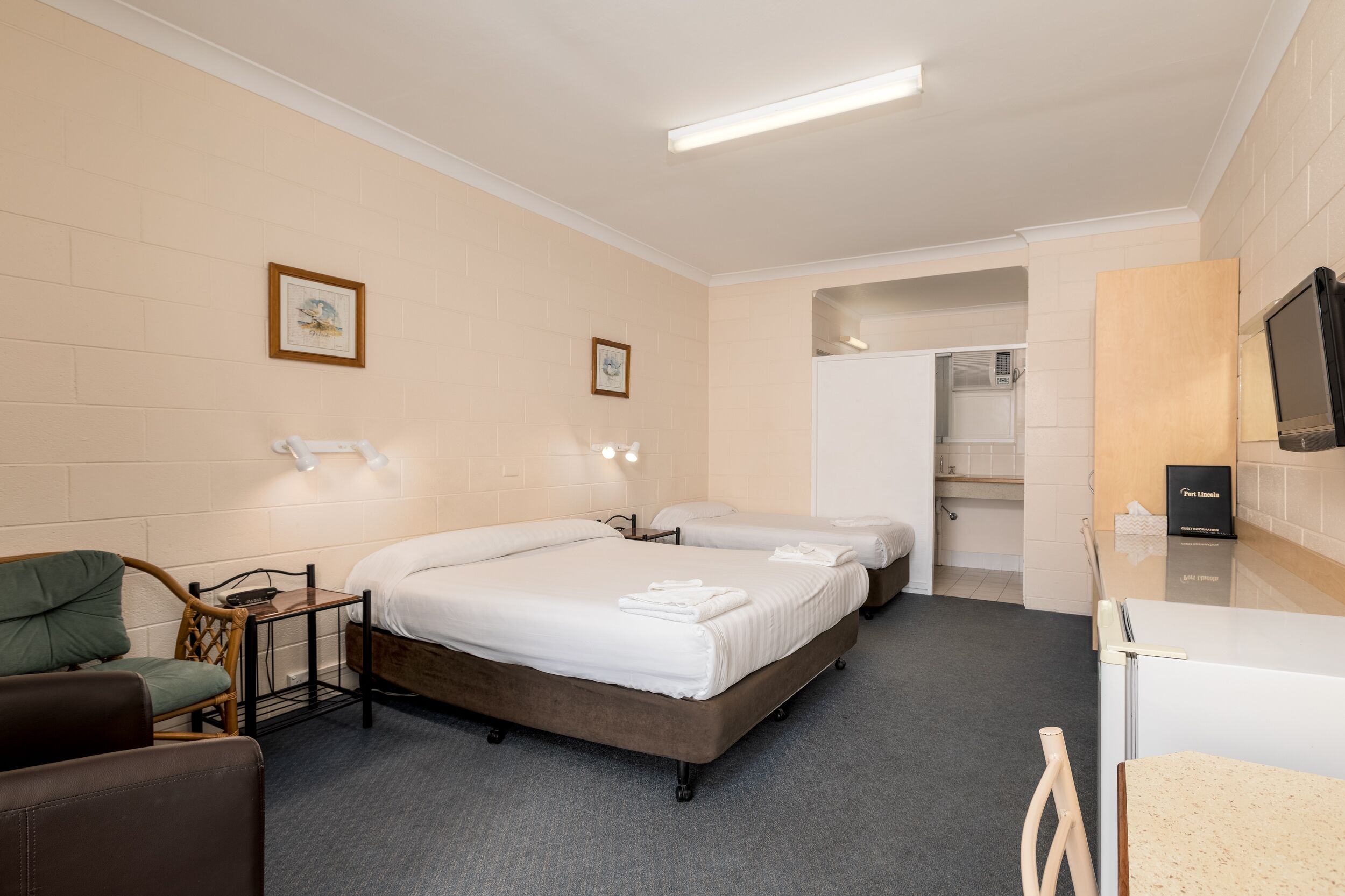 Una camera d'albergo con due letti, un tavolino, una sedia, una televisione e un bagno parzialmente visibile da una porta aperta.