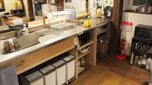 Una cocina con un lavamanos, estufa y diversos utensilios. Hay un extintor y un reloj en la pared.