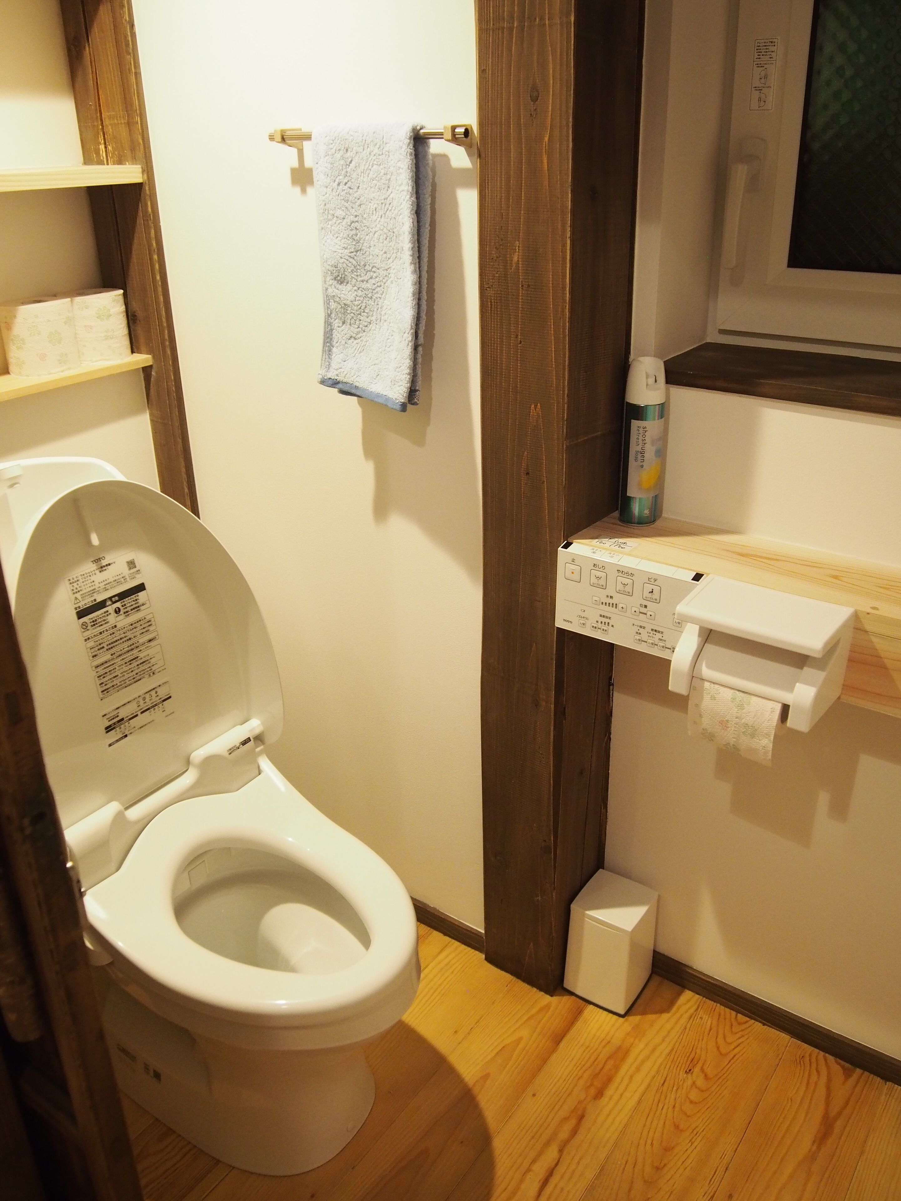A standard bathroom with a toilet, a towel rack, a paper towel dispenser, and a wooden shelf.