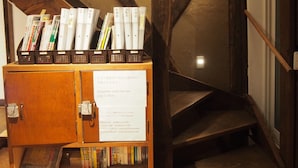 Una escalera de madera con estanterías a ambos lados, un banco de madera y un cartel con información de Wi-Fi y contraseña.