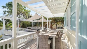 En overdækket terrasse med spisebord og stole, omgivet af hvide gelændere og et pergola.