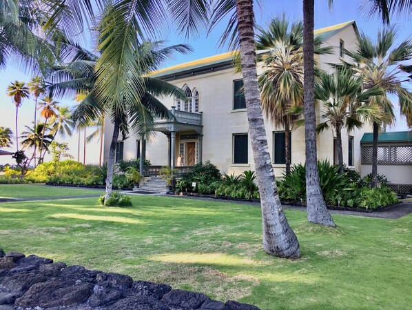 A two-story building with a balcony, surrounded by palm trees and well-maintained lawns.