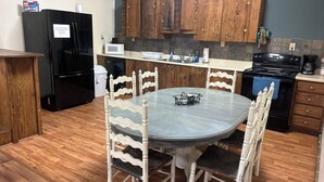 A kitchen with wooden cabinets, a black refrigerator, a microwave, a stove, and a dining table with chairs.