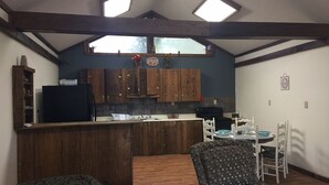 A compact kitchen with wooden cabinets, a black refrigerator, and a dining area with patterned chairs and a table.