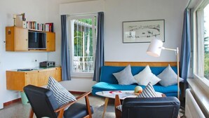 Una sala de estar moderna con un sofá azul, sillas negras, un aparador de madera y un ventanal con cortinas.