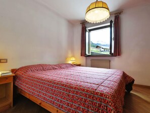 Ein Schlafzimmer mit einem großen Bett, einem Fenster mit Vorhängen, einer Nachttischlampe und Blick ins Freie.