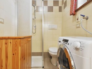 Ein kleines Badezimmer mit einem Holzkosmetikschrank, einer Waschmaschine, einer Toilette und einer Dusche.