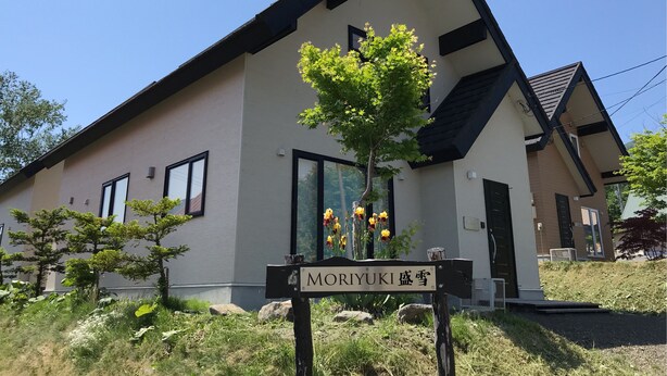Una casa moderna de dos pisos amb un disseny minimalista, amb grans finestres i un arbre petit al jardí davant.
