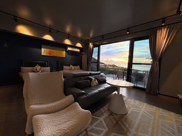 Une chambre d’hôtel moderne dotée d’un grand lit, d’un canapé, d’un fauteuil et d’un balcon offrant une vue sur la mer.