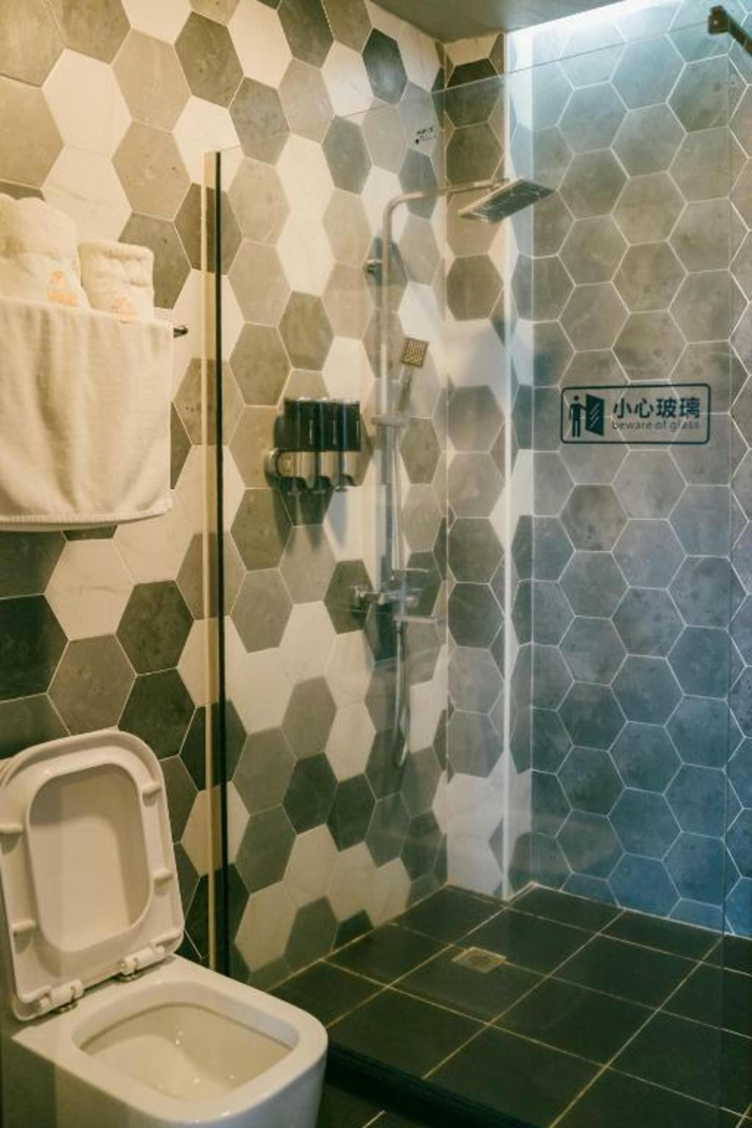A bathroom with a hexagonal tile wall, a toilet, a shower area, and a towel rack.