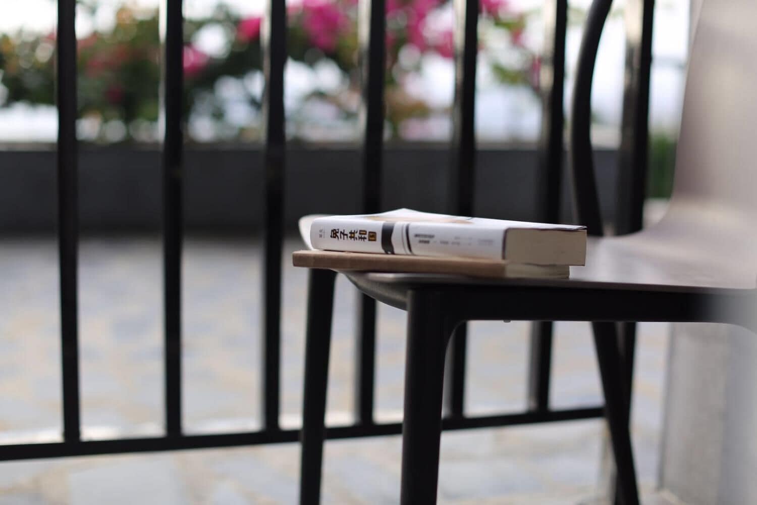 A chair with a book on it, positioned near a window with a view of flowers.