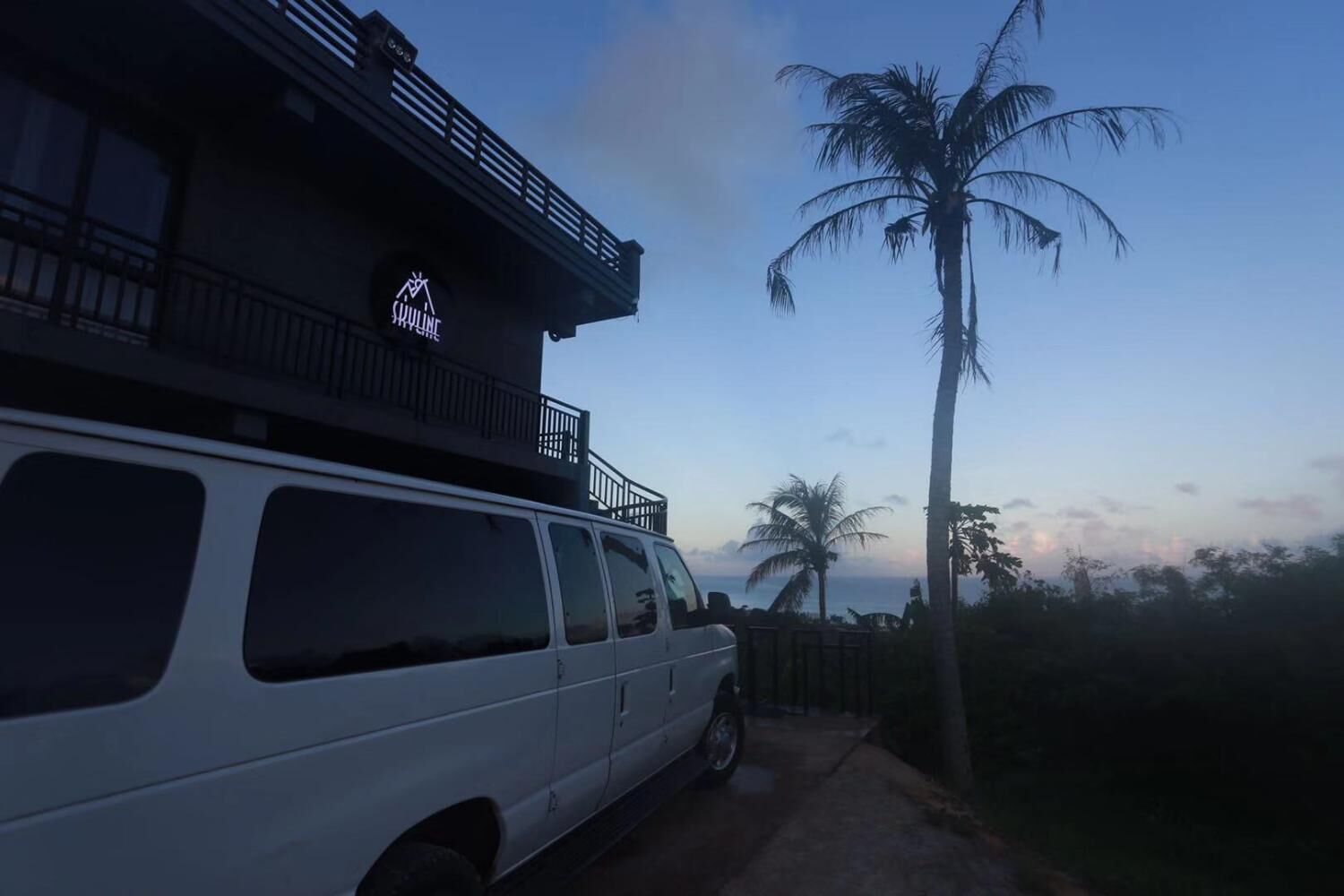 A white van parked in front of a building with a balcony and a sign that reads "SKYLINE".