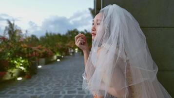 Une personne vêtue d’une robe de mariée, debout près d’un chemin de pierre bordé de verdure et de fleurs.