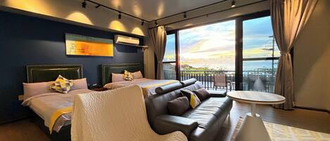 A modern hotel room with two beds, a sofa, a small table, and a balcony with a view.