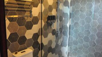 Casa de banho com padrão de azulejos hexagonais, cabine de duche em vidro e sanita.