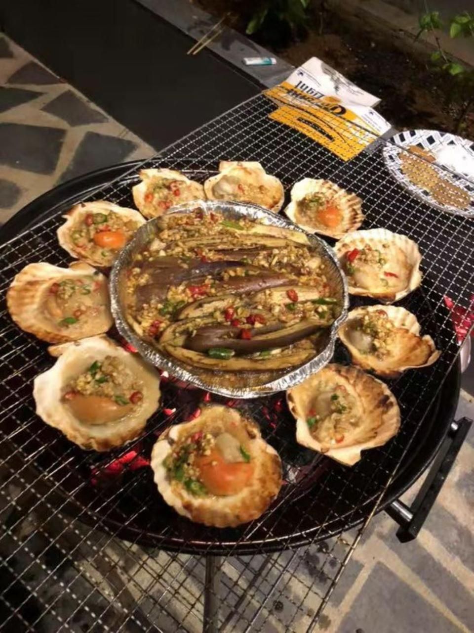 A grill with various seafood items, including oysters and a large fish, surrounded by a wire table.