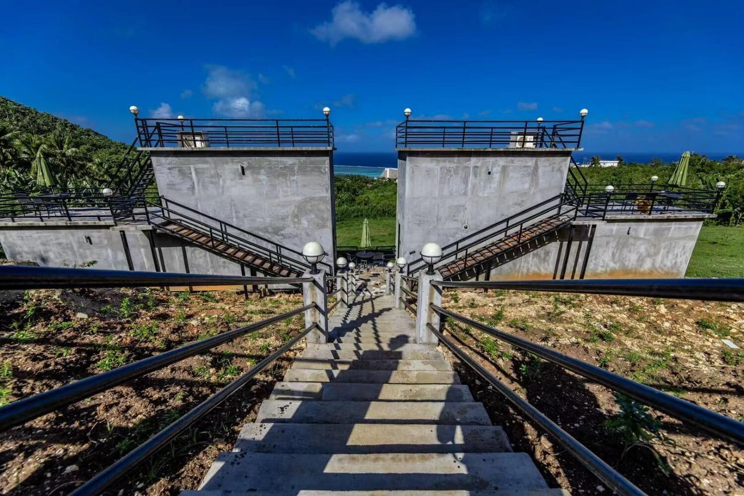 A staircase leading to a concrete structure with railings and lamp posts, overlooking a coastal area.