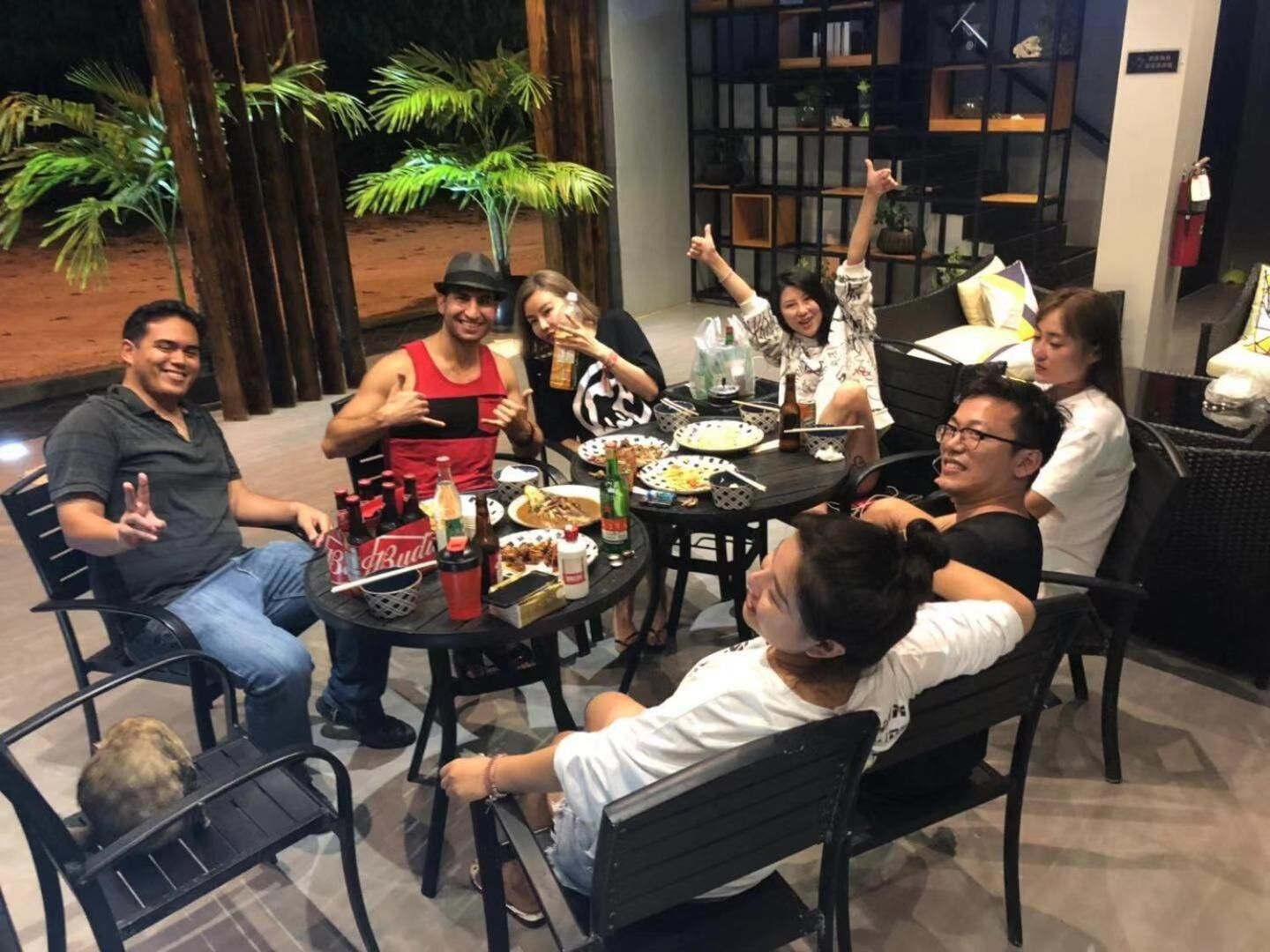 Un groupe de personnes est assis autour d’une table, devant de la nourriture et des boissons, dans une pièce au design moderne, agrémentée de plantes.