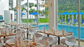 A dining area with tables set for service, large windows with a view of a pool and greenery, and a ceiling with a ship's wheel design. - AVI Pangkor Beach Resort (Pangkor Island)