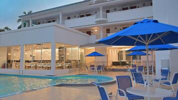 Ein Poolbereich eines Hotels mit blauen Sonnenschirmen, Liegestühlen und einem Essbereich mit Tischen und Stühlen.