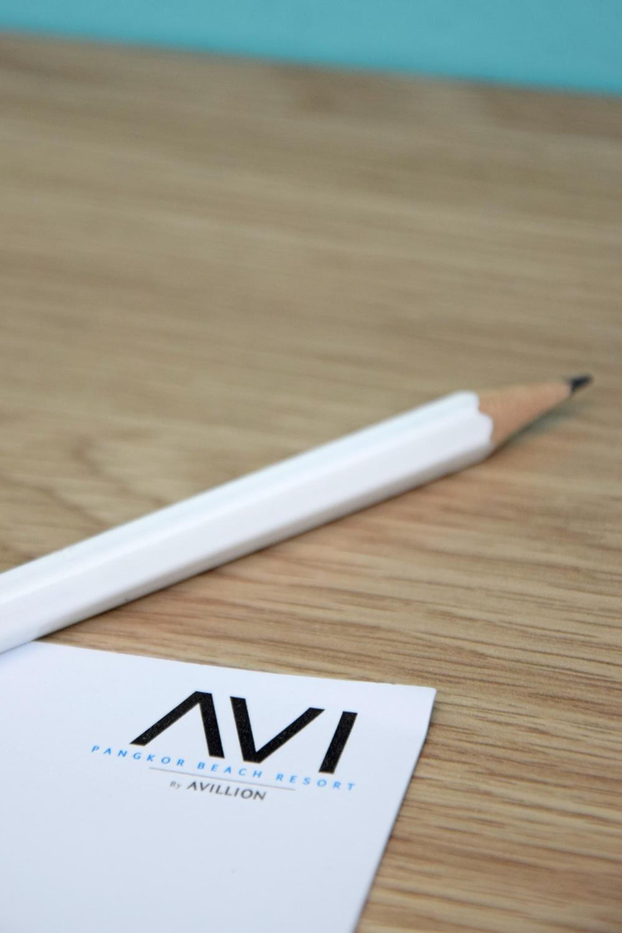 A white paper with the text "AVI PANGKOR BEACH RESORT" and a white pencil on a wooden surface.