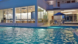 A modern hotel with a swimming pool, large glass windows, and outdoor seating. - AVI Pangkor Beach Resort (Pangkor Island)