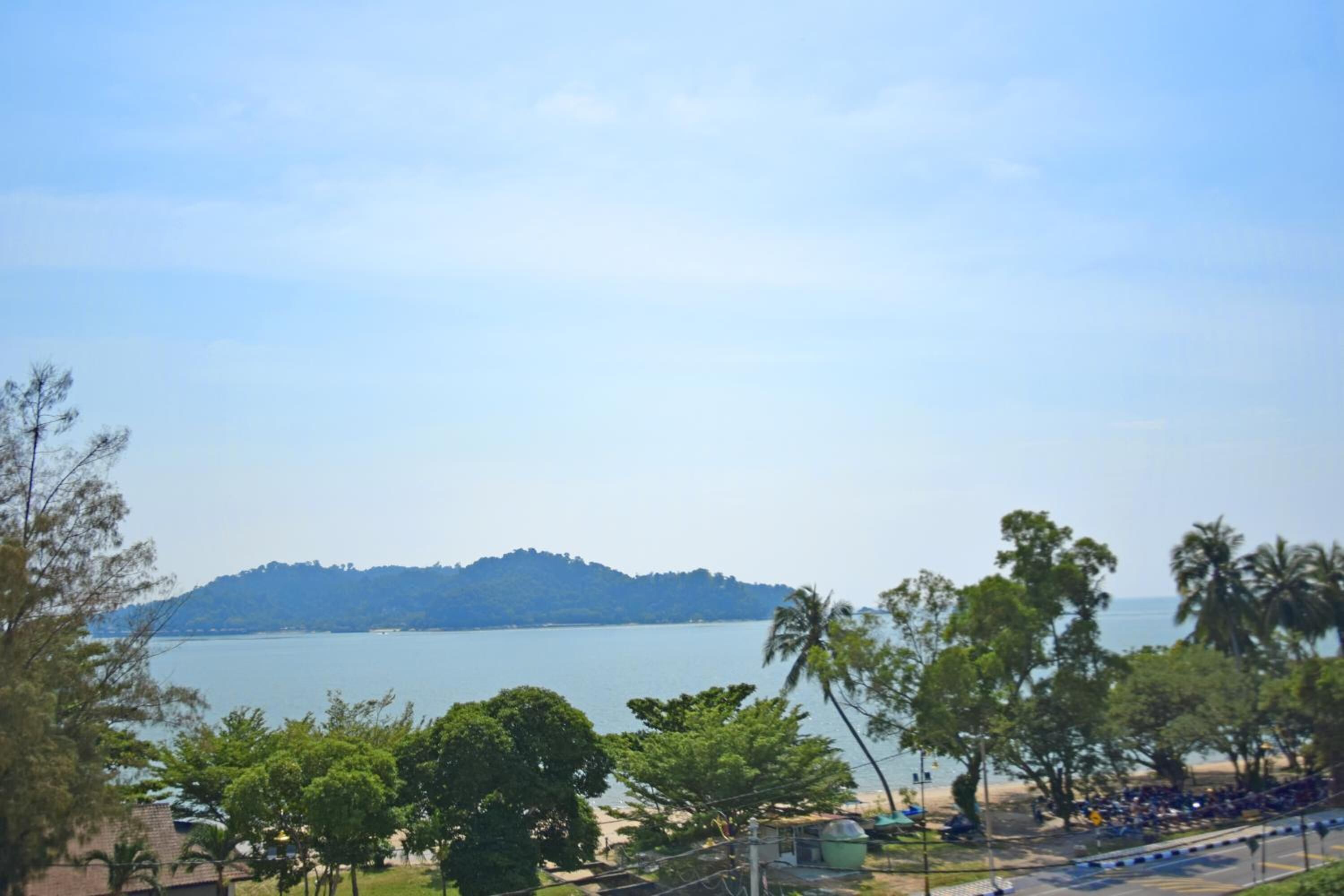 A beach view with a clear sky, trees, and a distant hill.