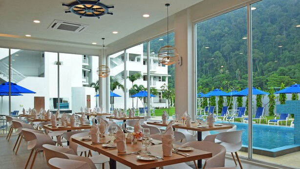 A restaurant with tables set for dining, large windows offering a view of a pool and greenery. - AVI Pangkor Beach Resort (Pangkor Island)