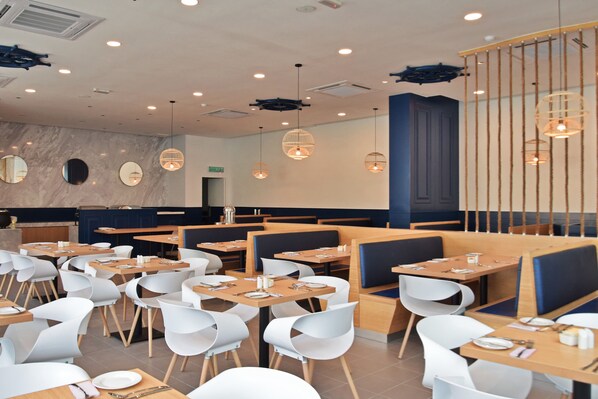 Un restaurant moderne avec des tables rondes, des chaises blanches et des banquettes bleues.