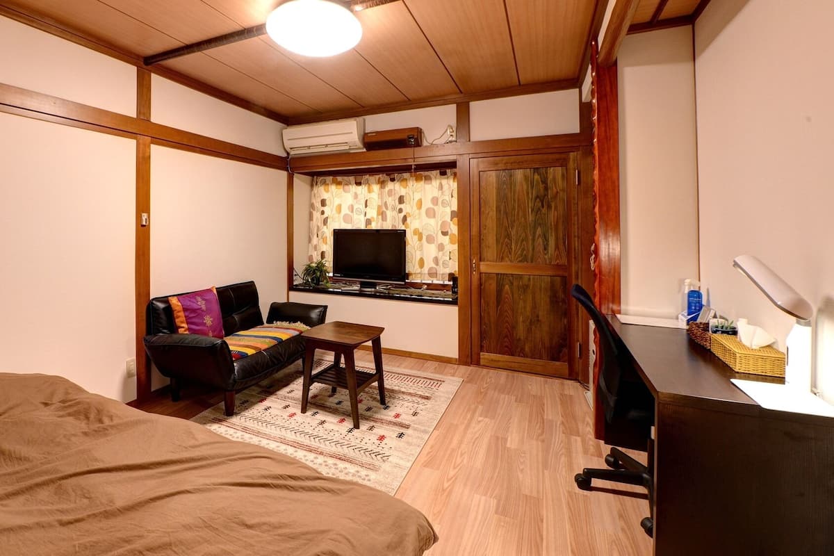 Una habitación pequeña con cama, sofá, escritorio, televisor y armario.