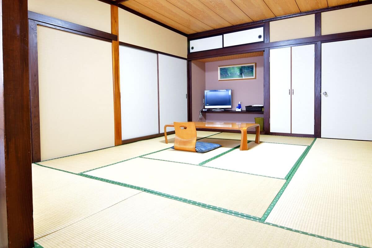 Una habitación tradicional japonesa con suelo de tatami, una mesa de madera baja, un televisor y puertas correderas.