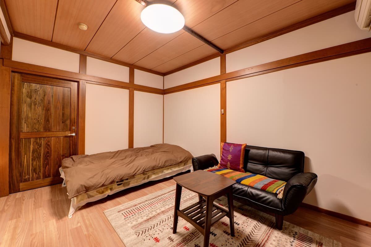 Una habitación pequeña y acogedora con techo de madera, una cama, un sofá de cuero negro y una pequeña mesa.